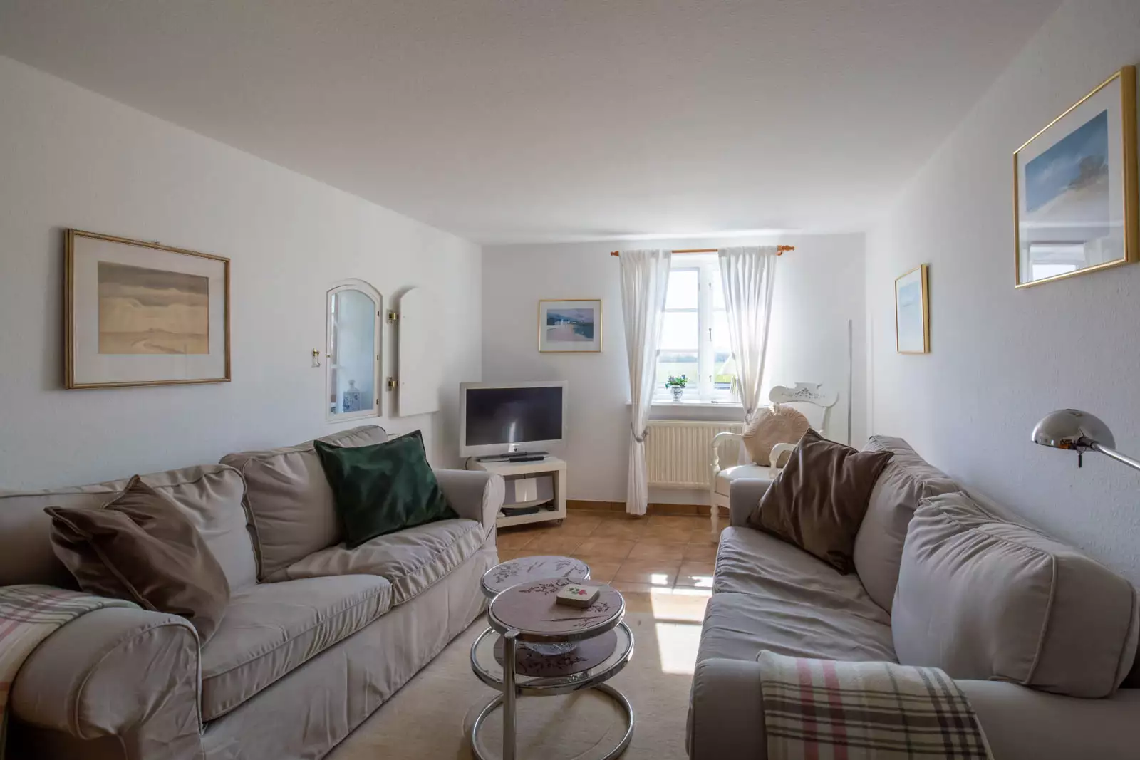 Heller Wohnbereich der Ferienwohnung Nordermühle auf Pellworm mit zwei Sofas, Couchtisch, Fernseher und sonnigem Fenster