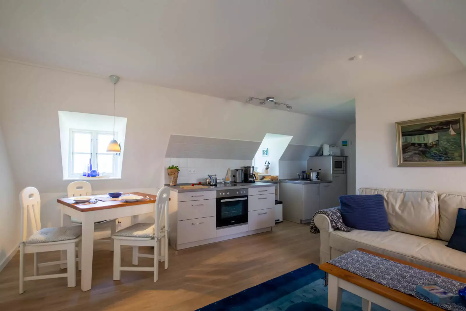 Offener Wohnraum der Ferienwohnung Leuchtturm auf Pellworm mit Couchecke, Essbereich, Küchenzeile und sonnigen Fenstern