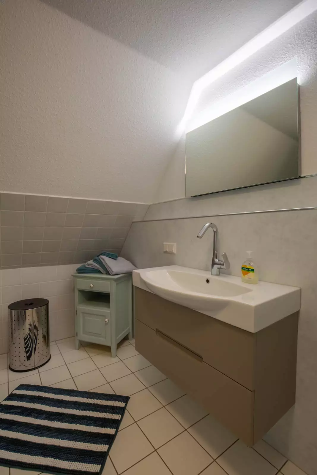 Badezimmer der Ferienwohnung Leuchtturm auf Pellworm mit Waschbecken und beleuchtetem Spiegel