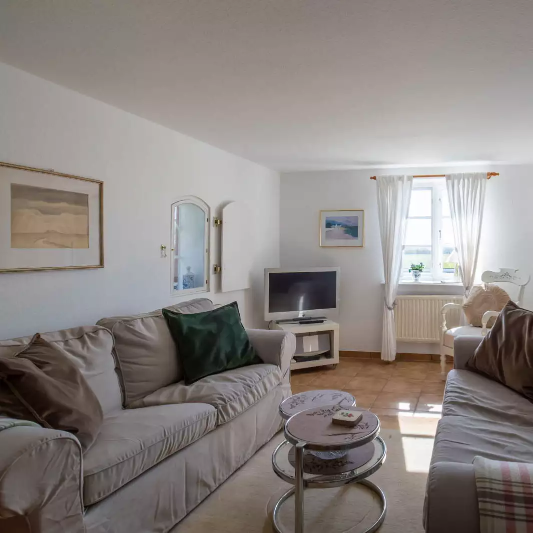 Wohnzimmer der Ferienwohnung Nordermühle auf Pellworm mit Sofas, Couchtisch, Fernseher und hellem Fenster