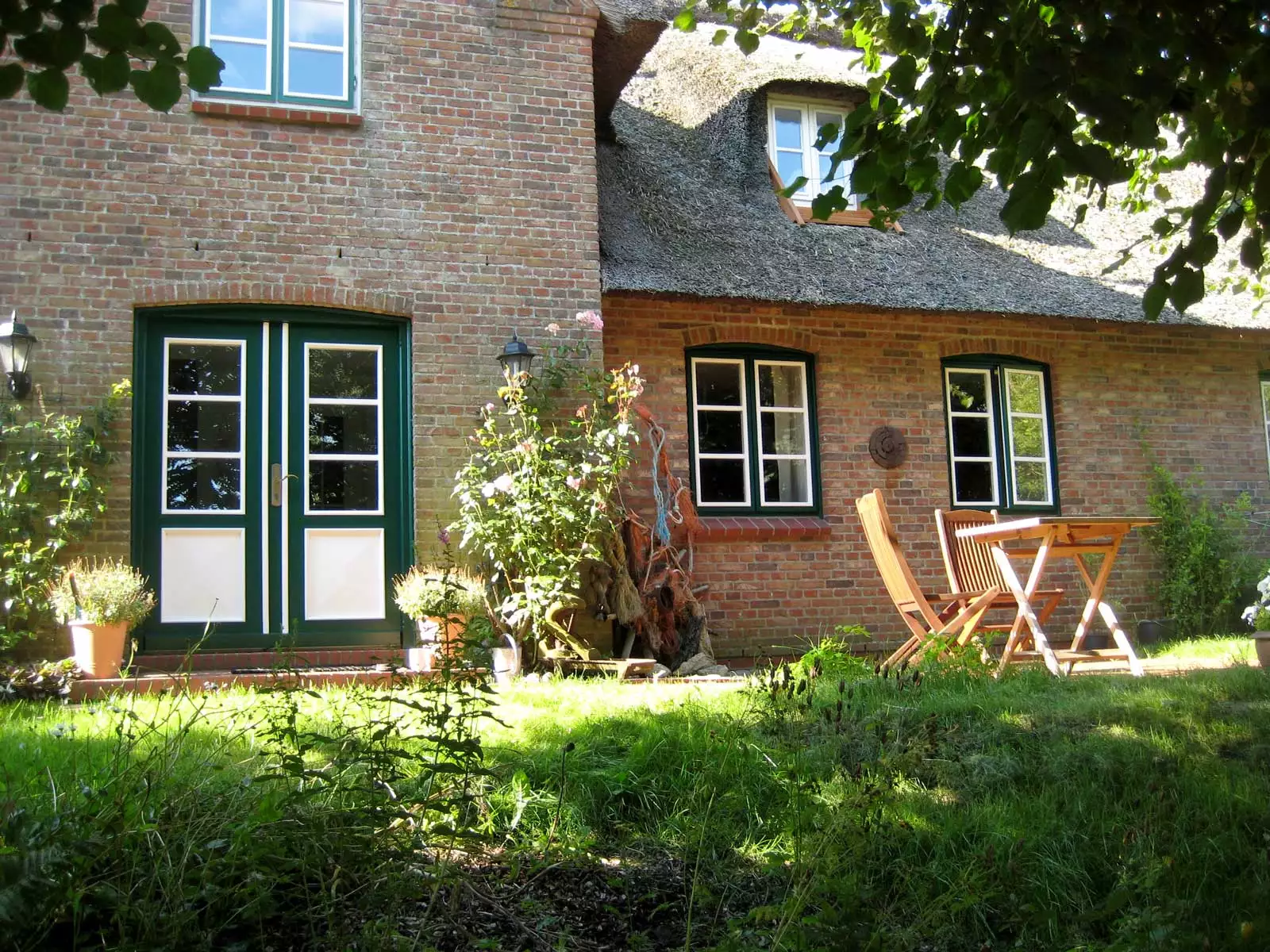 Rückseite des Reetdach-Ferienhauses Kiek in’t Land auf Pellworm mit Terrasse, Gartenmöbeln und Sonnenschein